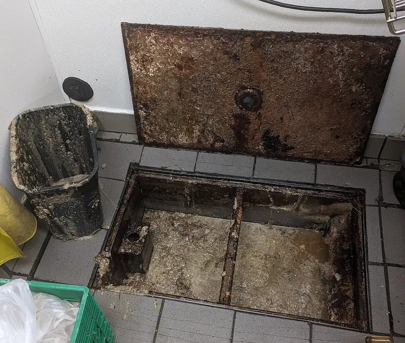 Caixa de gordura aberta no piso de uma cozinha