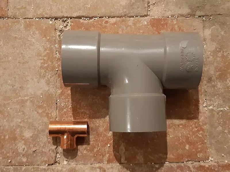 Tê de PVC cinza ao lado de um tê de cobre